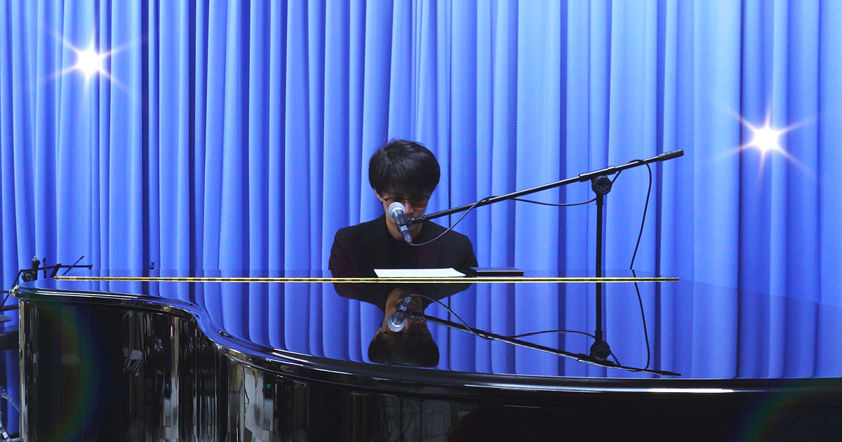 神戸市中央区・三宮の100BANスタジオにて、藤澤遼が桑田佳祐の楽曲をピアノで演奏している場面です。演奏に集中する様子とスタジオの空気感が伝わる写真です。
